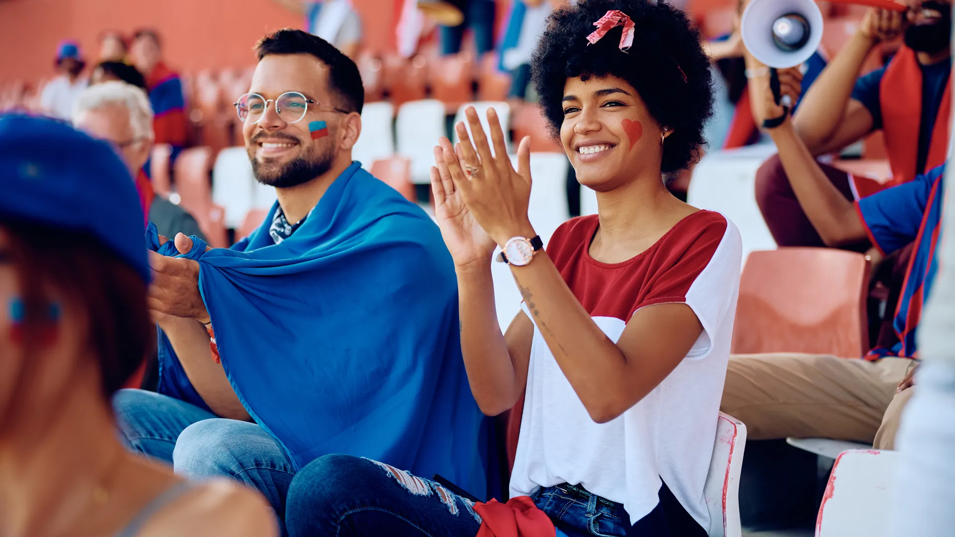Fans applauding while watching a sports game from stadium seats