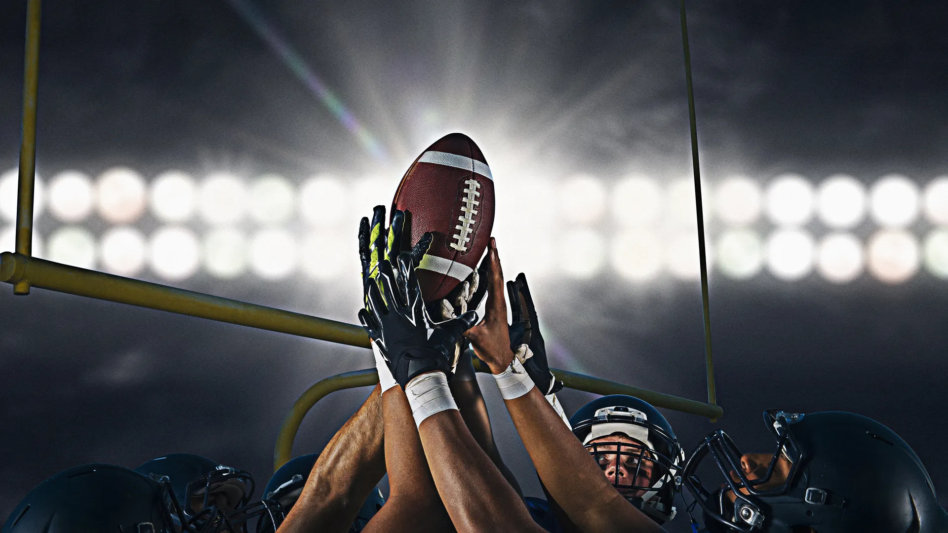 American football players reaching for a game-winning catch under stadium lights