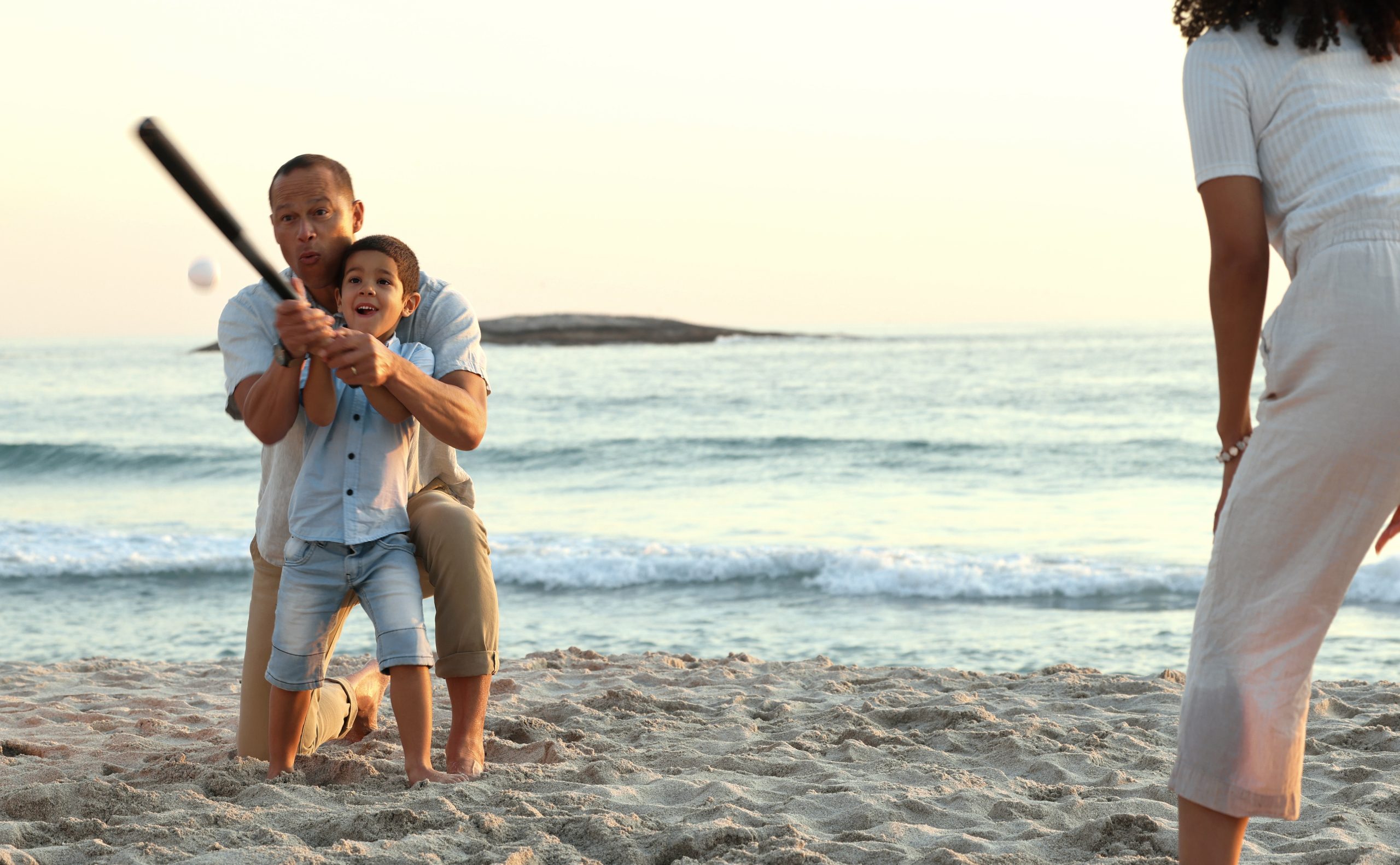 A family playing baseball together on a sunny beach by the ocean, illustrating a Clearwater spring training trip that doubles as a beach vacation.