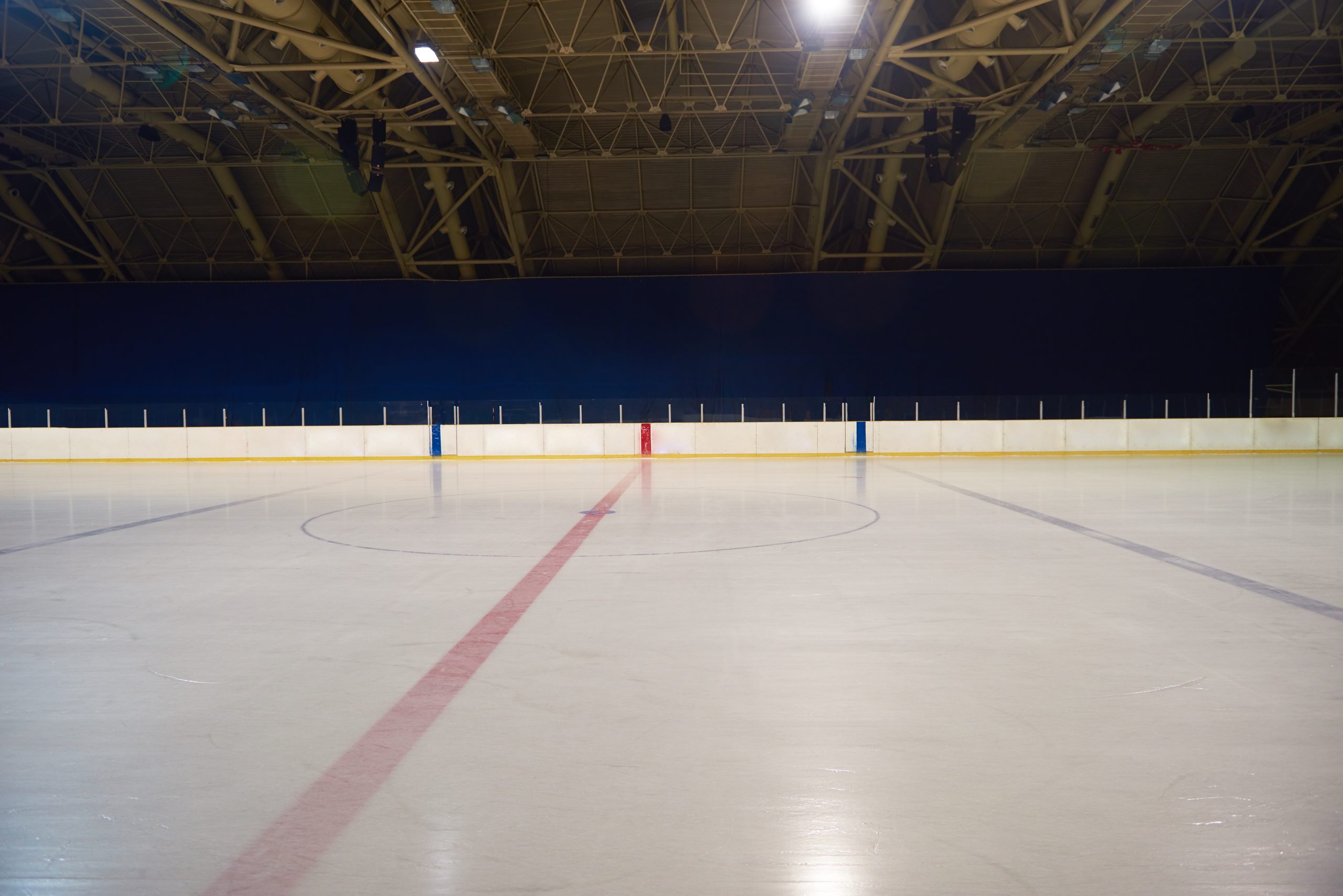 Empty ice hockey rink and dasherboards inside a darkened indoor arena