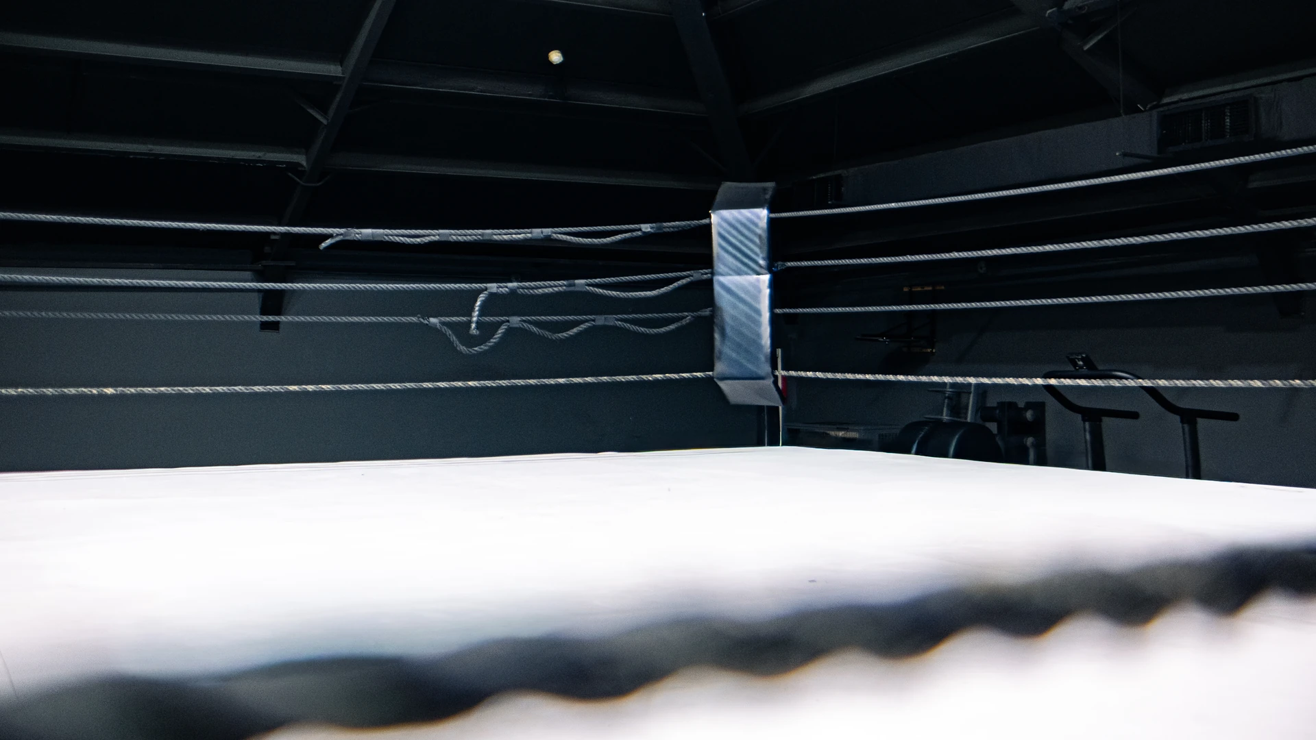 Empty boxing ring with pale canvas, dark ropes and a padded corner