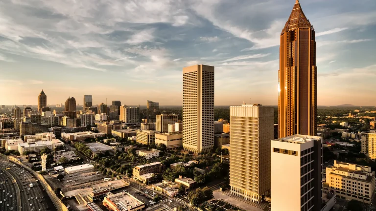 Downtown Atlanta at golden hour: a copper-toned skyscraper with a pyramid-shaped top on the right, more towers beyond it and a busy highway at lower left